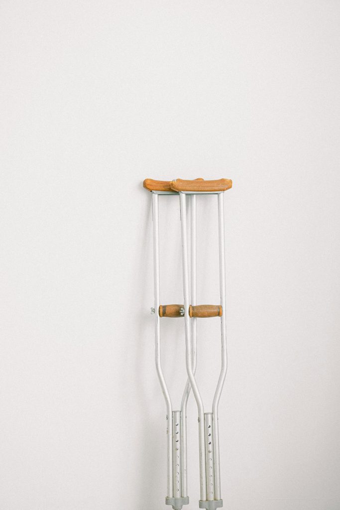 Minimalist image of crutches leaning on a white wall indoors.